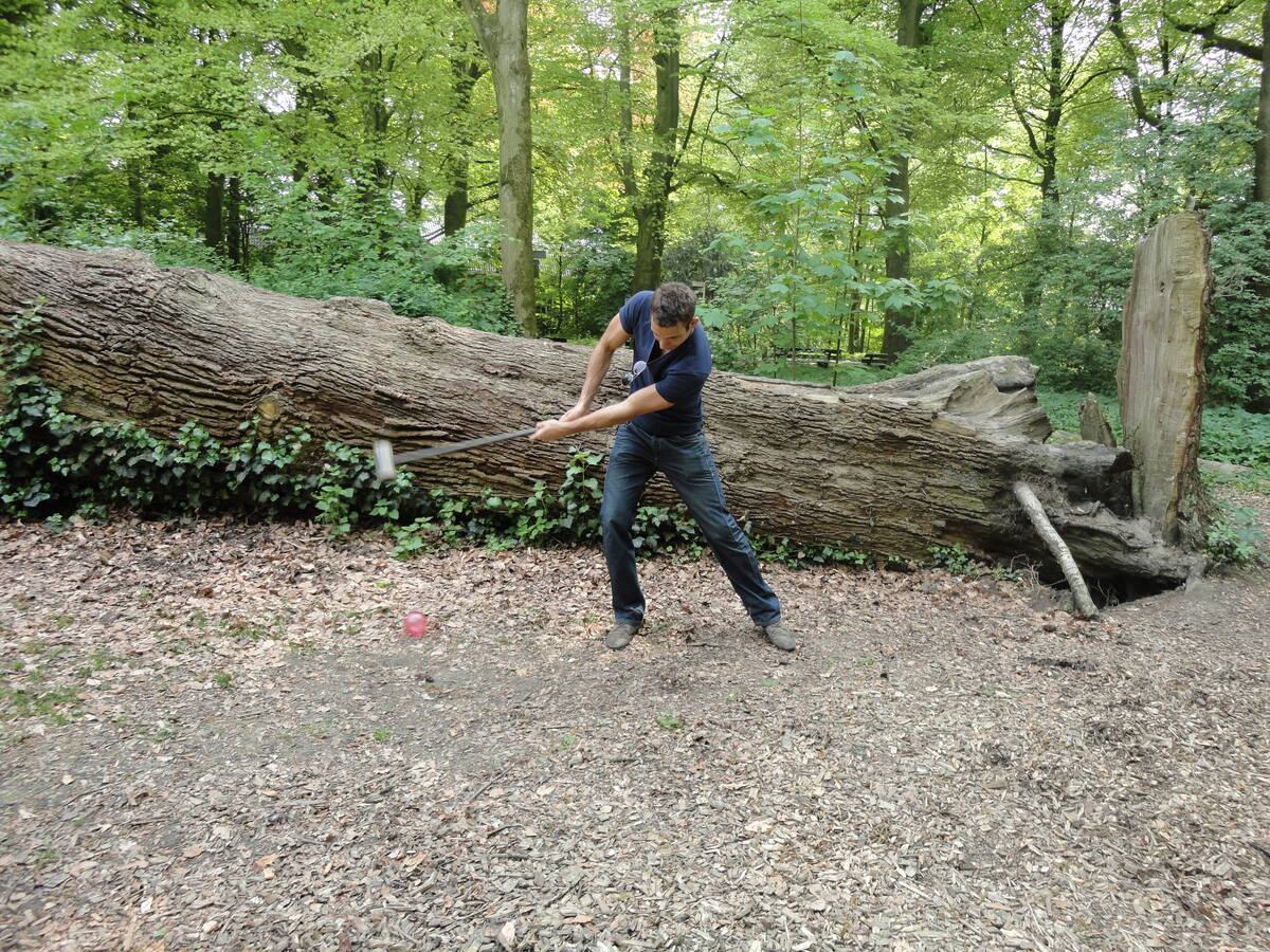 Deelnemer slaat met volle swing de bal weg tijdens bosgolf bij een omgevallen boom