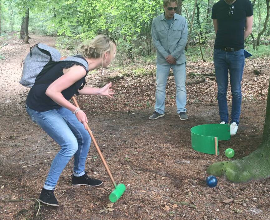 Speelster mikt de bal richting de hole terwijl teamgenoten toekijken tijdens bosgolf in het bos