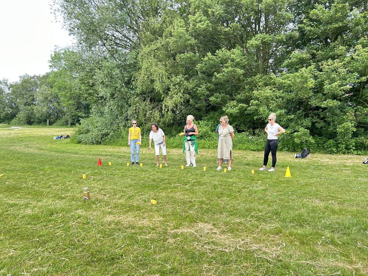 Vier spelers werpen tegelijk hun werpstokken tijdens Kubb in de tuin